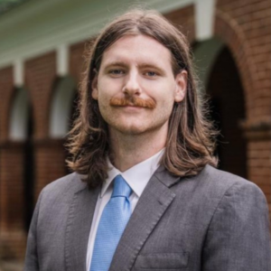 Headshot of Trevor Hamilton in a suit and tie posing on UVA's grounds